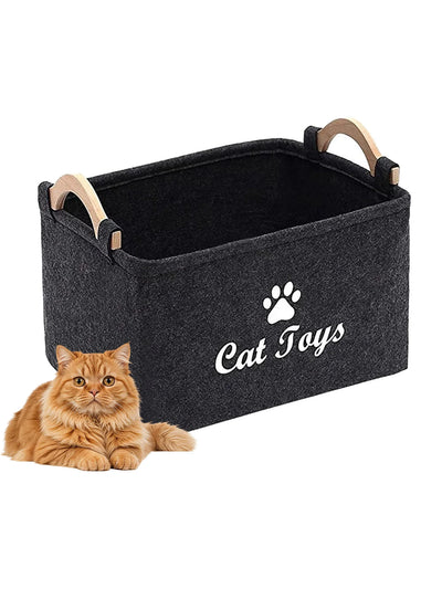 Aviour black pet accessories storage basket labeled Cat Toys with wooden handles next to a fluffy orange cat